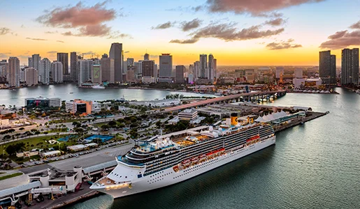 Cruise ship docked with Miami skyline at sunset.
